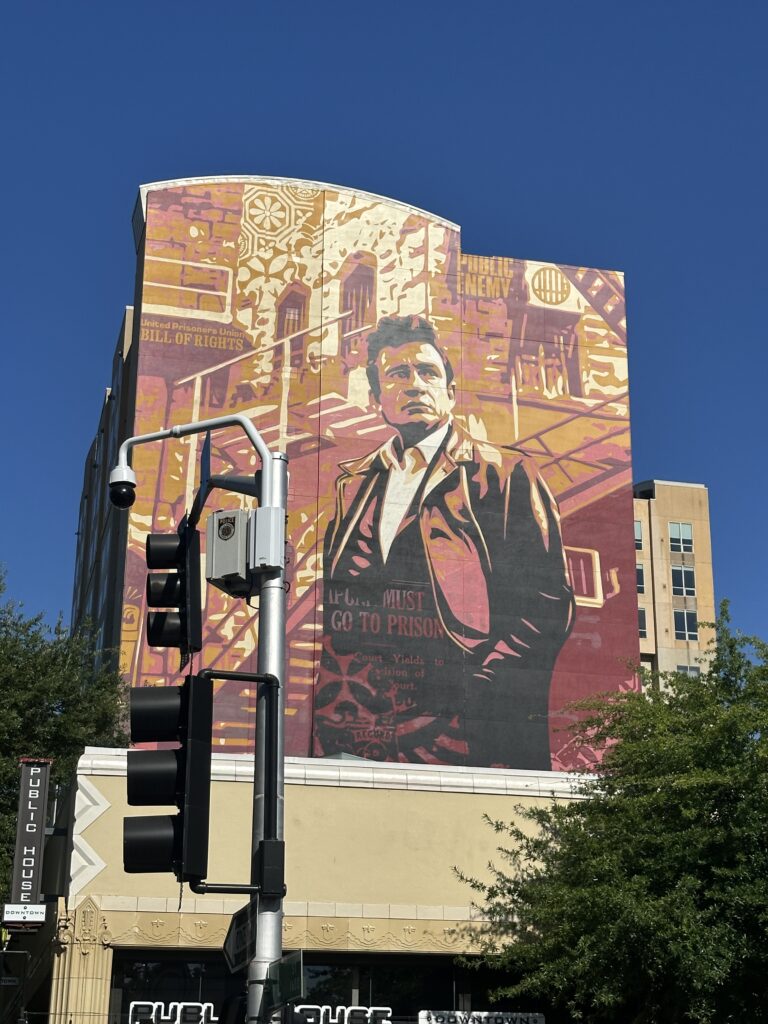 Large outdoor mural in downtown Sacramento featuring a stylized portrait of Johnny Cash against a red and gold background, with the words 'PUBLIC ENEMY' and 'Bill of Rights.